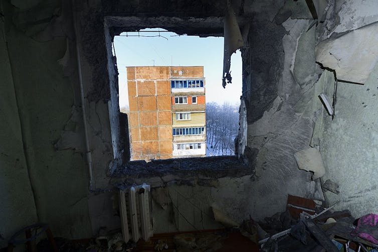 The view of a damaged-looking apartment building from inside another damaged apartment.