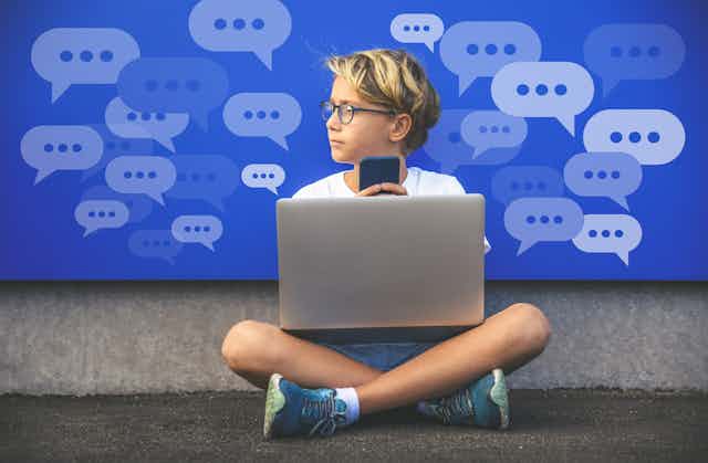A boy with a laptop and holding a cell phone looks to the left. Conversation bubbles with dots are in the background.