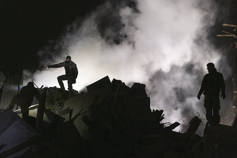 Three Ukrainian rescue workers surrounded with smoke and silhouetted against the night sky.