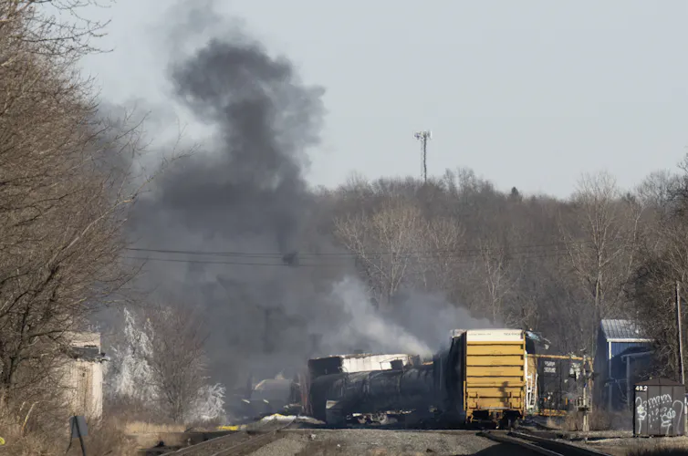 Photo de wagons du train déraillé dont s’élève un panache de fumée noire