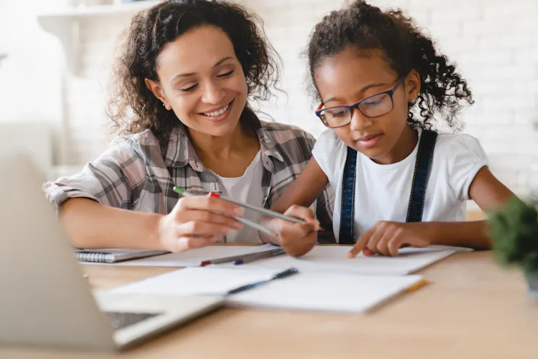 A woman helps a young girl with her schoolwork.
