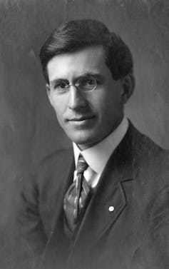 Black and white portrait of man wearing small glasses.