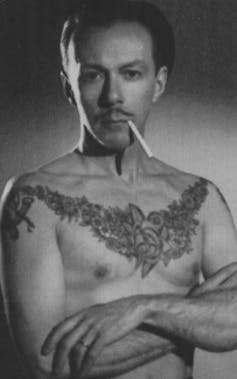 Shirtless tattooed man smoking a cigarette.