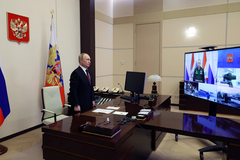 Vladimir Putin stands behind his desk watching a new nuclear submarine being launched on a video screen.