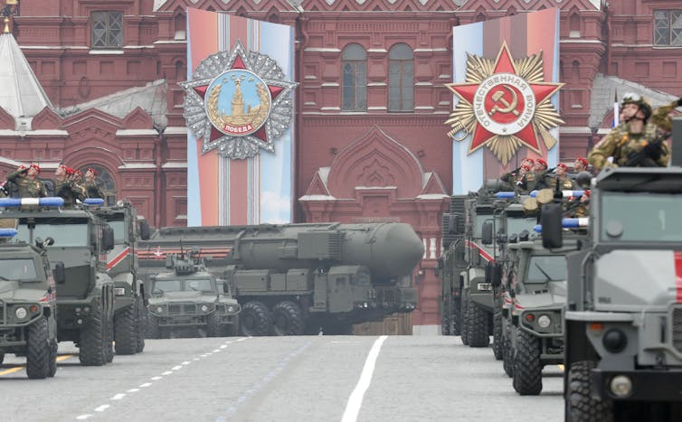 Tanks and a missile launch drive past a red building with Soviet banners.