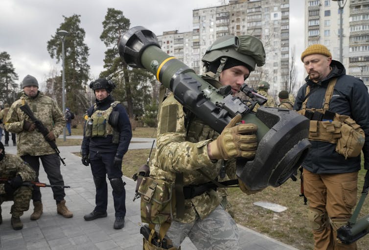 A group of soldiers on a city street with the soldier in the foreground holding a long tube over his shoulder