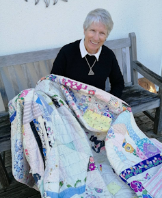 A woman sits on a bench carrying a quilt