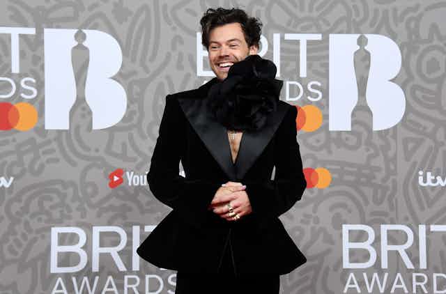 Harry Styles wearing a black suit with a peplum waist and a giant flower choker necklace at the Brit Awards