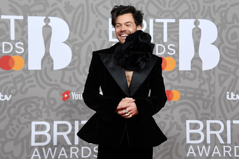 Harry Styles wearing a black suit with a peplum waist and a giant flower choker necklace at the Brit Awards
