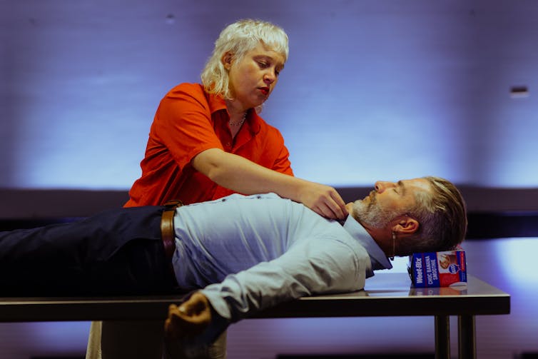 A woman in red stands over a man lying down.