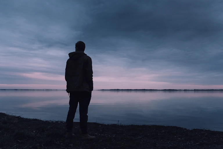 A young man looks at a lake.