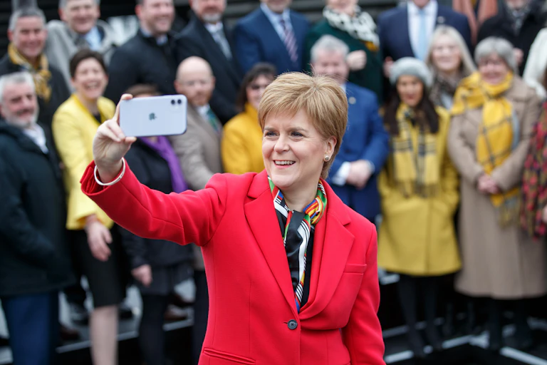 Nicola Sturgeon holds her iphone up to take a selfie, with other MSPs in a group behind her
