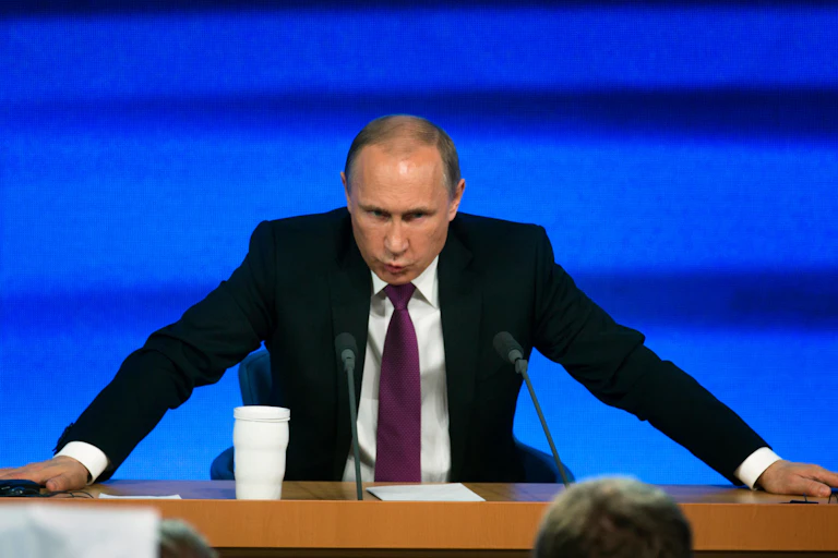 A man in a suit and tie leans forward on a desk.