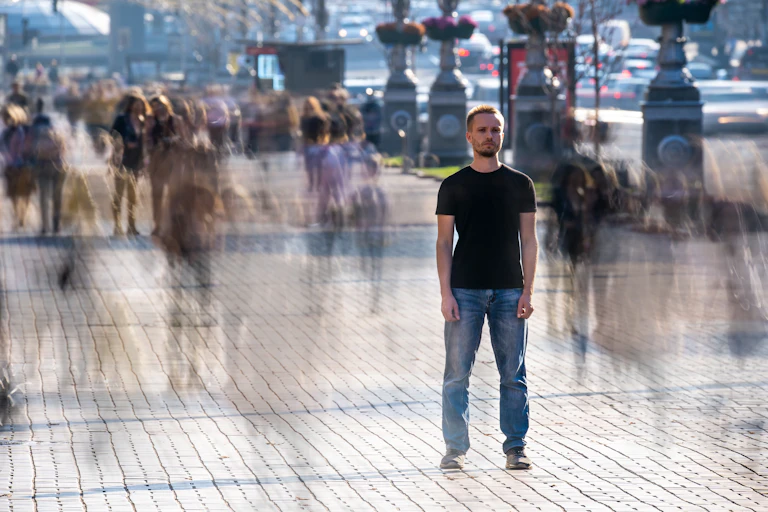A man stands in the street amid a passing crowd