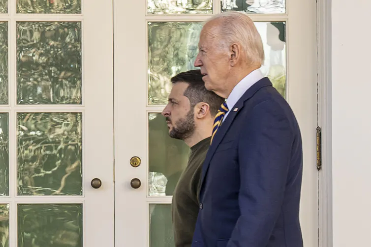 Two men walk past a white door.