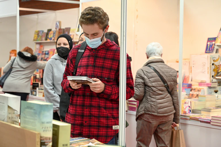 A young man in a mask reading a poetry book in a bookshop.