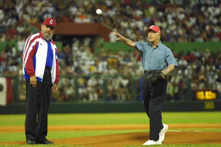A man is watching another man throw a baseball in front of a crowd of people in a stadium.