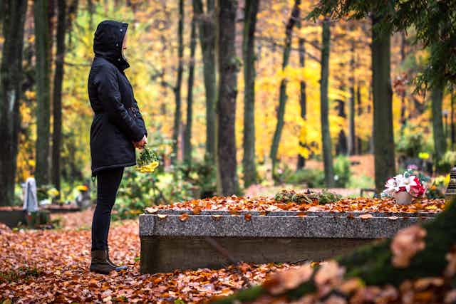 Photo d’une femme se recueillant devant une tombe, par une journée d’automne.
