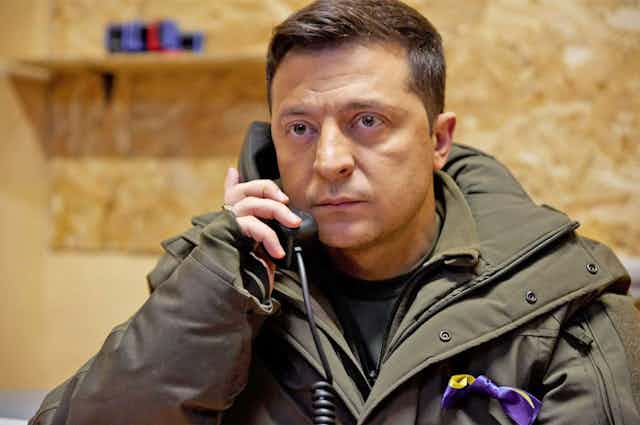 A man staring at the camera holding a telephone.