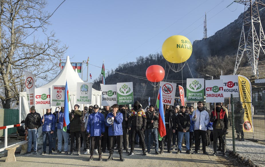 A crowd carrying 'Save nature' signs and balloons stands against a mountain backdrop