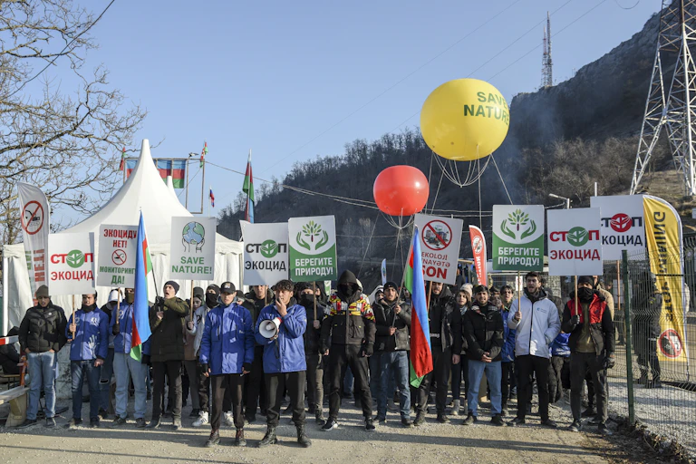 A crowd carrying 'Save nature' signs and balloons stands against a mountain backdrop