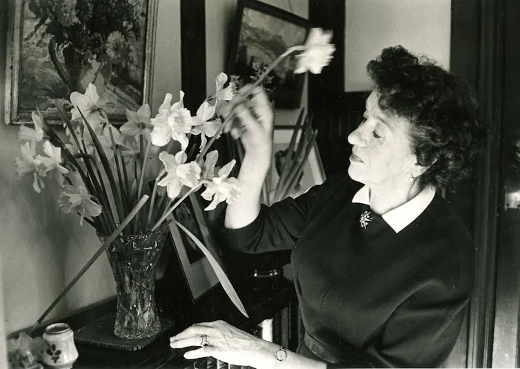 Black and white photograph shows Enid Blyton arranging daffodils in a vase.