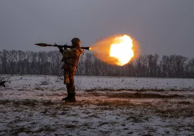 A ball of fire erupts after a solider fires his weapons that is held on his shoulder. 