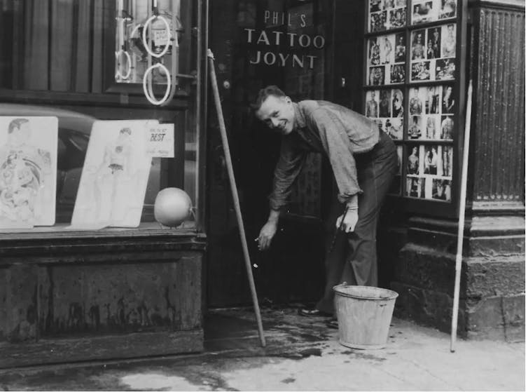 Samuel washes the window of Phil's Tattoo Joynt, black and white photo