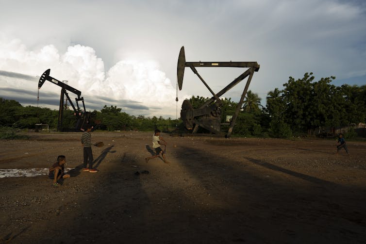 two children play baseball with two large oil wells