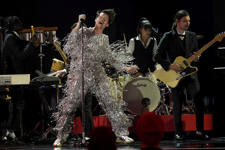 Harry Styles performing on stage wearing a metallic silver fringed onesie by Gucci