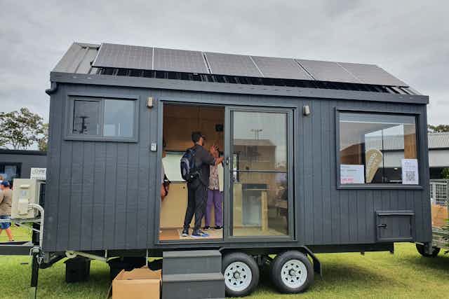 View from outside of a tiny house on a trailer with dark timber cladding and solar panels