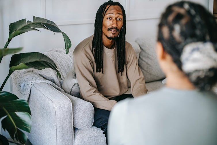 Man with dreadlocks sitting on sofa talking to therapist