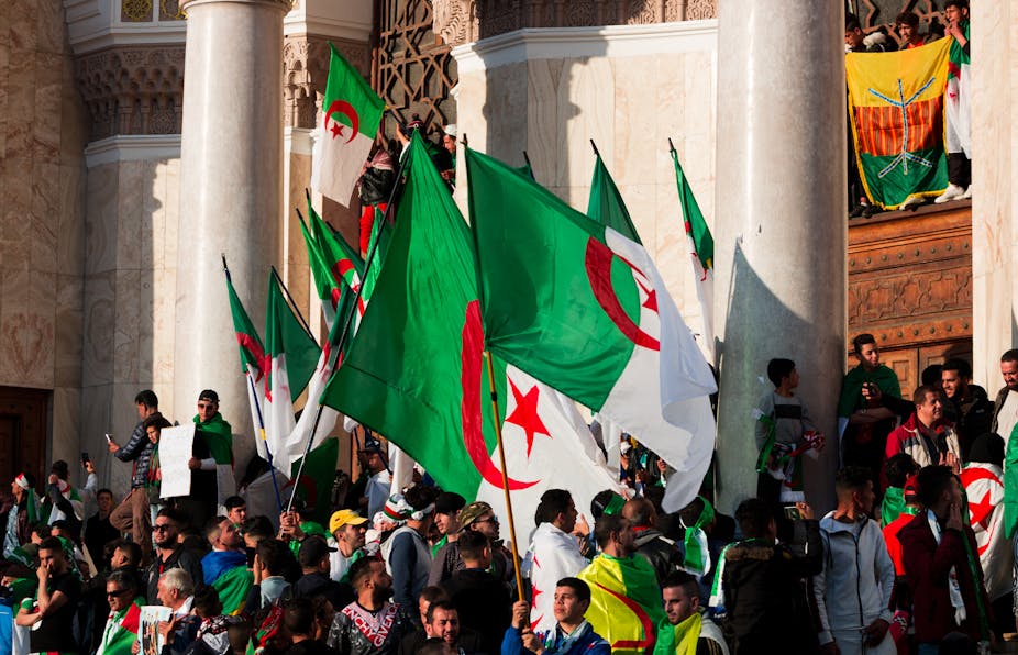 Une foule manifeste avec des drapeaux algériens. 
