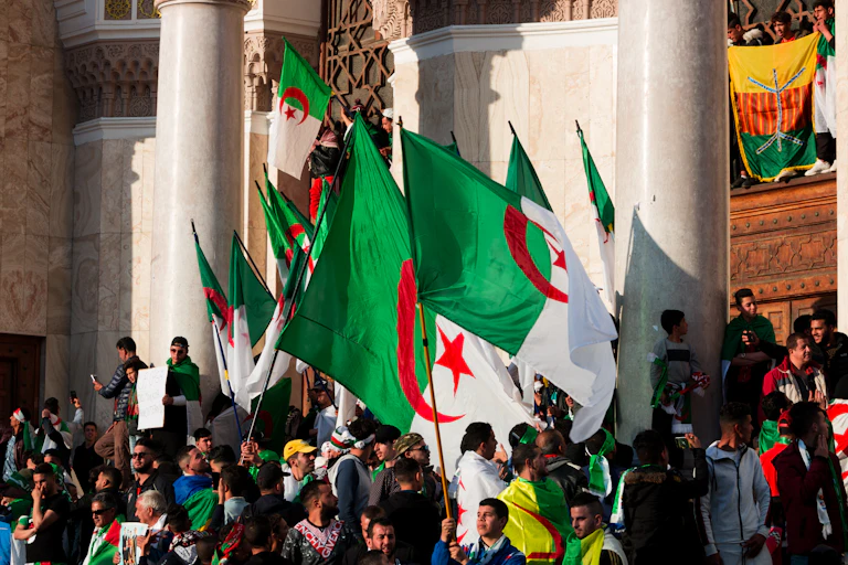 Une foule manifeste avec des drapeaux algériens.