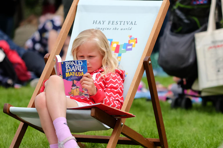 A young girl reads Matilda by Roald Dahl on a deck chair.