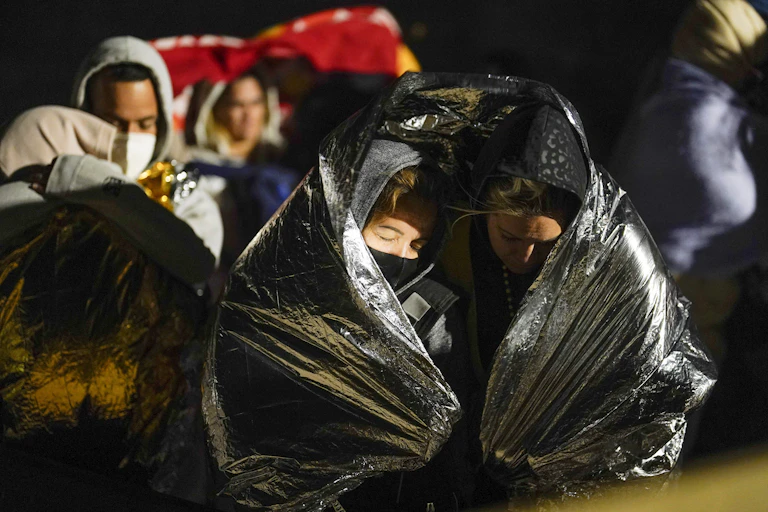 Two people huddle under a plastic sheet at nighttime.