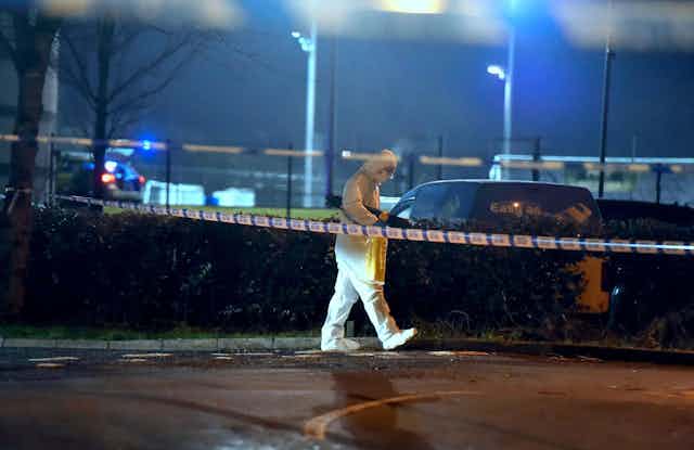 A man in a forensic suit walks behind a police cordon at the scene of the shooting of police officer John Caldwell. 