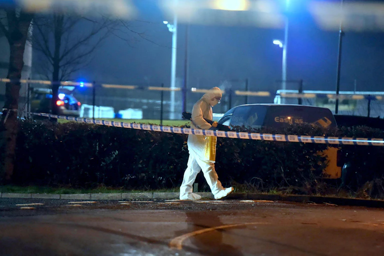A man in a forensic suit walks behind a police cordon at the scene of the shooting of police officer John Caldwell.