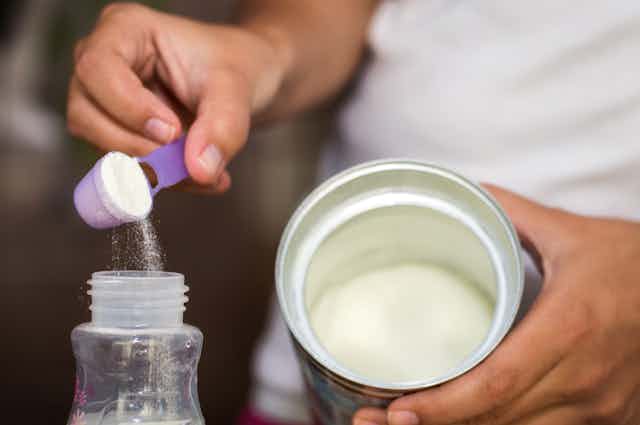 Photo d’une personne en train de préparer un biberon avec du lait en poudre