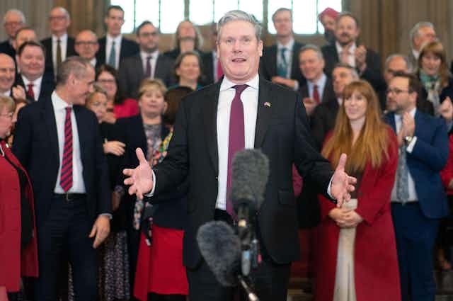 Keir Starmer speaking into a microphone with his MPs in the background.
