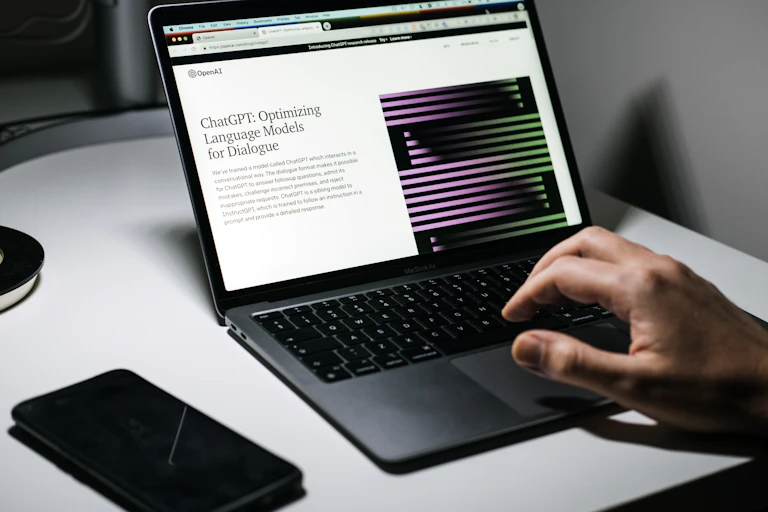A hand seen at a laptop on a ChatGPT screen.