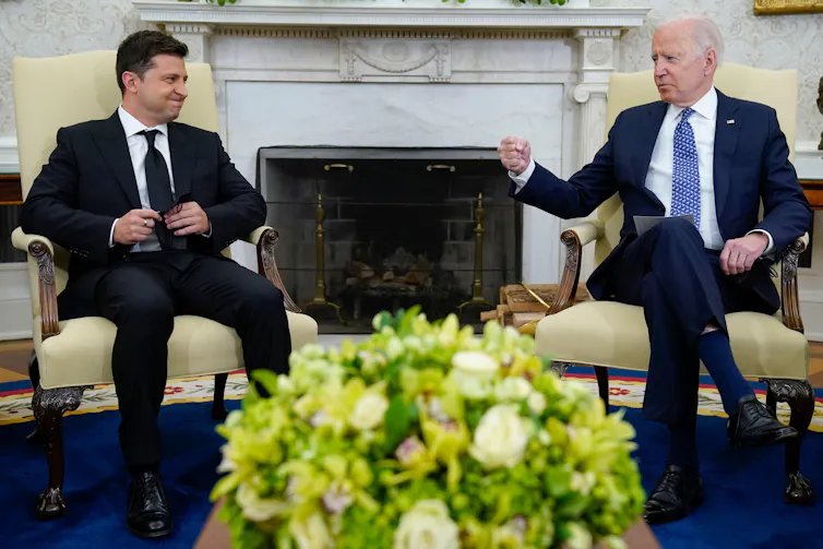 Two men in suits sitting in chairs.