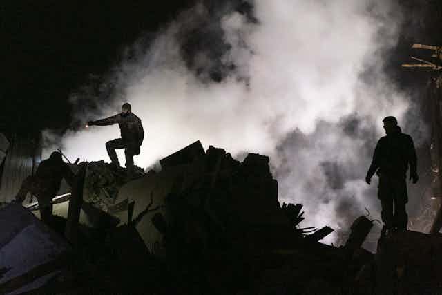 Tres socorristas ucranianos rodeados de humo y recortados contra el cielo nocturno.