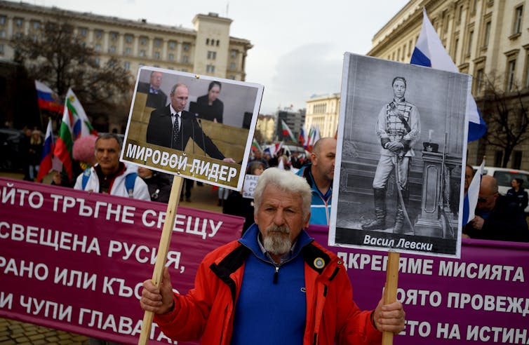 A man holds up two placards, one of Vladimir Putin one of Bulgarian revolutionary Vasil Levski