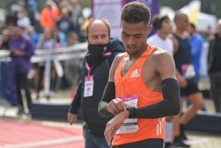 Runner wearing orange pinnie checks watch.