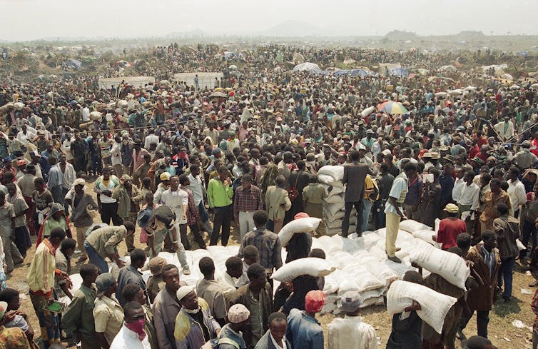 A crowd gathers around a pile of sacks containing food.