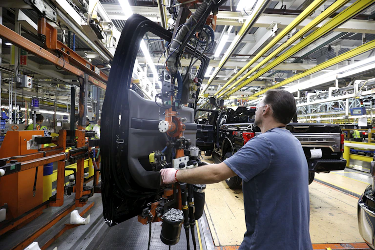 A worker maneuvers a truck door on an assembly line.