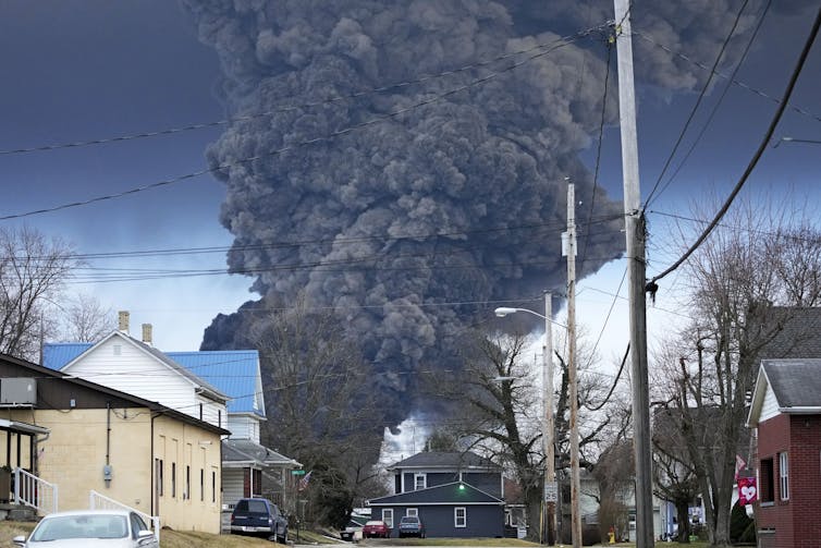 Houses are in the foreground as a large plume of smoke billows in the background