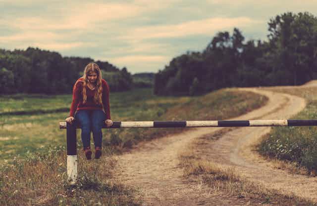 Young girl sitting on a fence in a field.