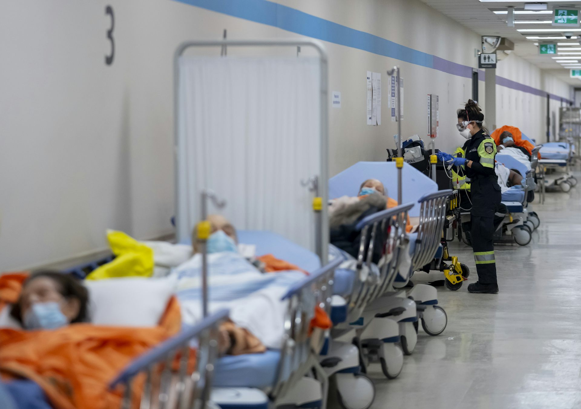 A long hallway with patients on gurneys along one wall, with a paramedic speaking to one of the patients
